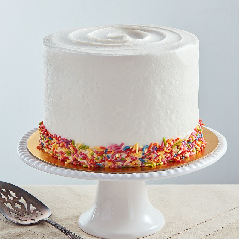 6-inch vegan French vanilla cake with smooth white buttercream frosting and a colorful sprinkle border on a white pedestal stand.