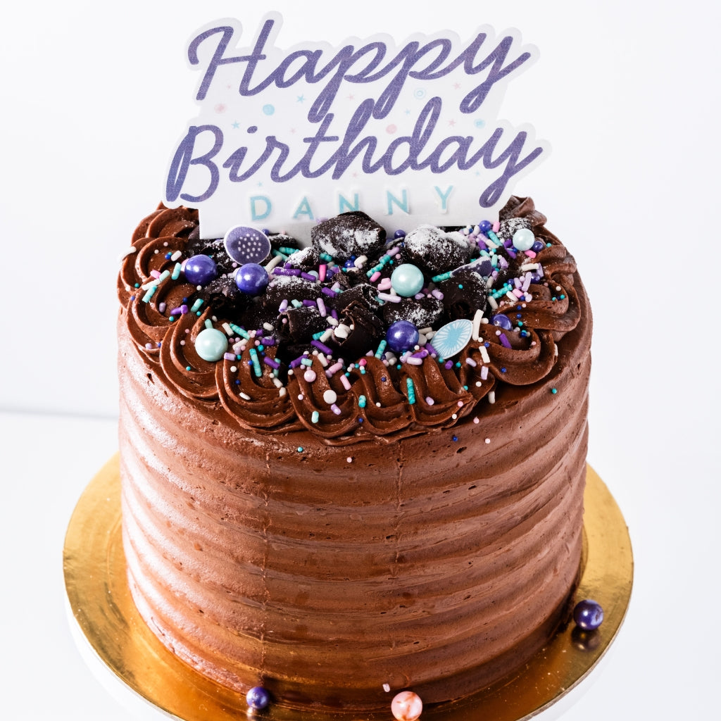 6-inch chocolate cake with velvety frosting, topped with chocolate shavings, colorful sprinkles, and a Happy Birthday topper.