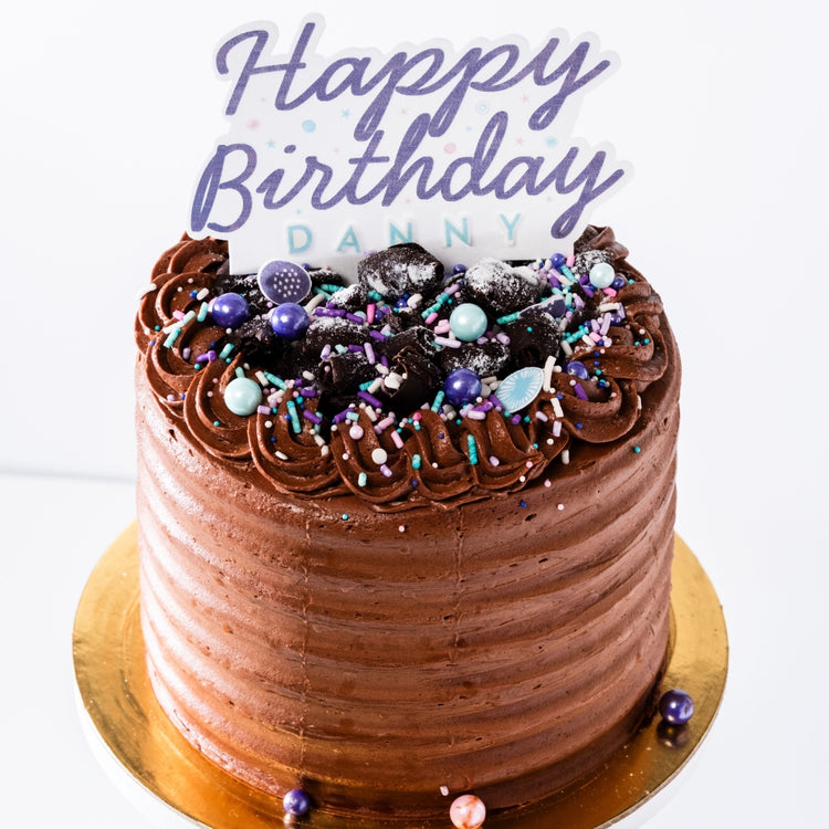 6-inch chocolate cake with velvety frosting, topped with chocolate shavings, colorful sprinkles, and a Happy Birthday topper.