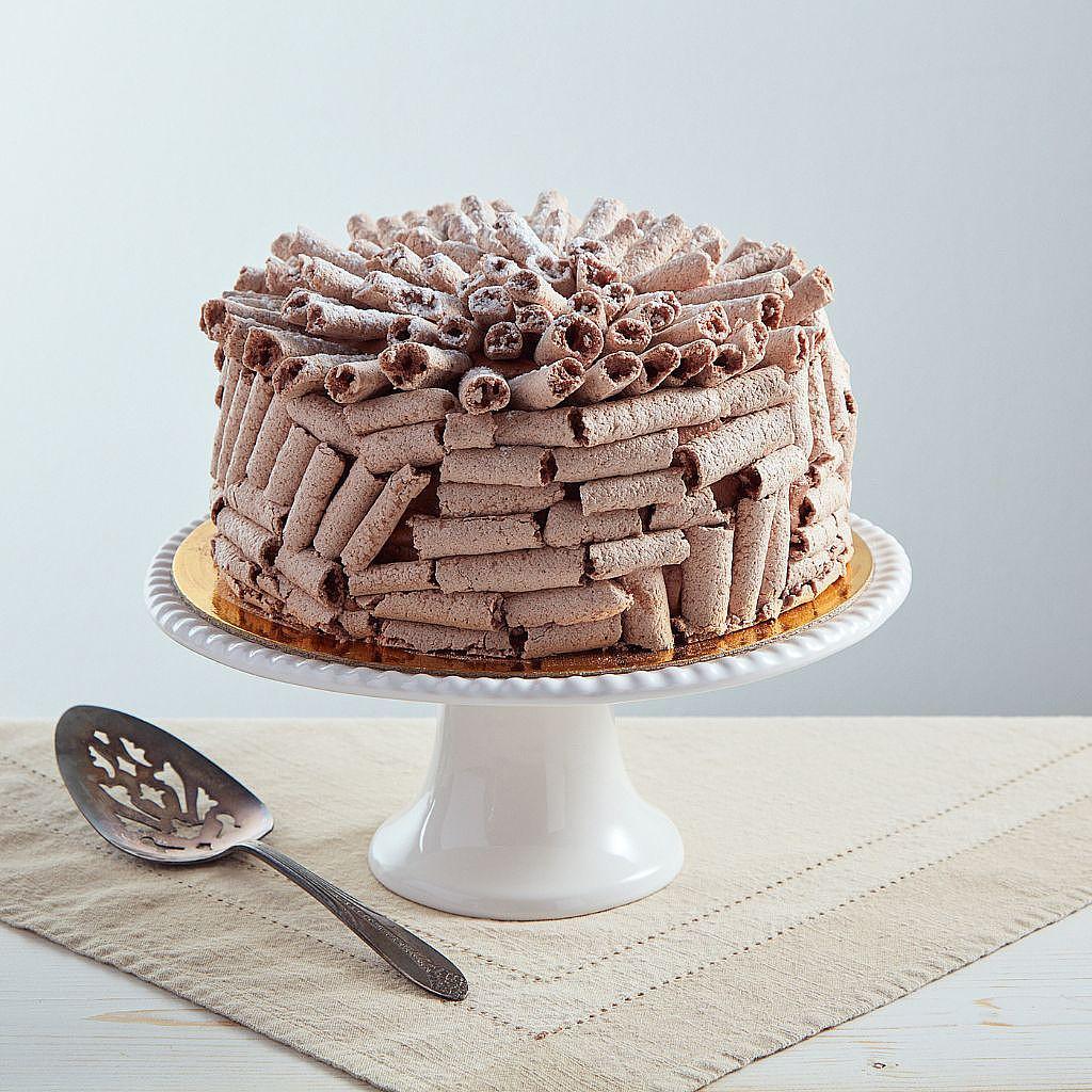 6-inch gluten-friendly chocolate Concorde cake covered in meringue curls on a white pedestal stand with a cake server.