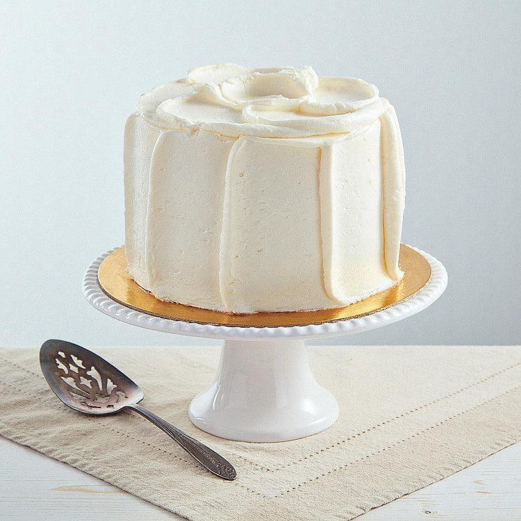 6-inch French vanilla cake with smooth white buttercream frosting on a white pedestal stand with a cake server.