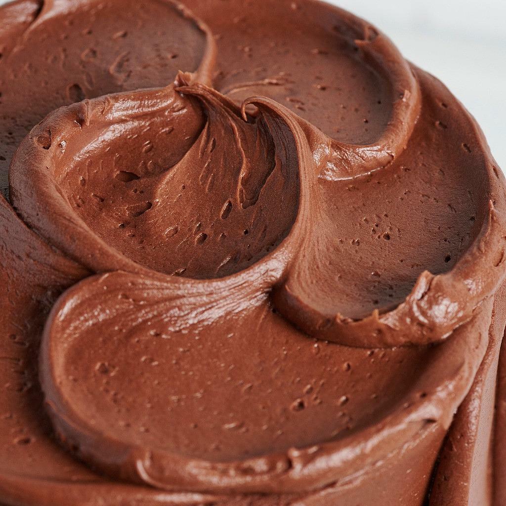 Close-up of a 6-inch golden cake topped with thick, swirled chocolate buttercream frosting.