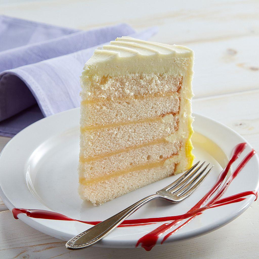 Slice of 6-inch lemon cake with white layers, lemon curd filling, and yellow ombre buttercream on a white plate.