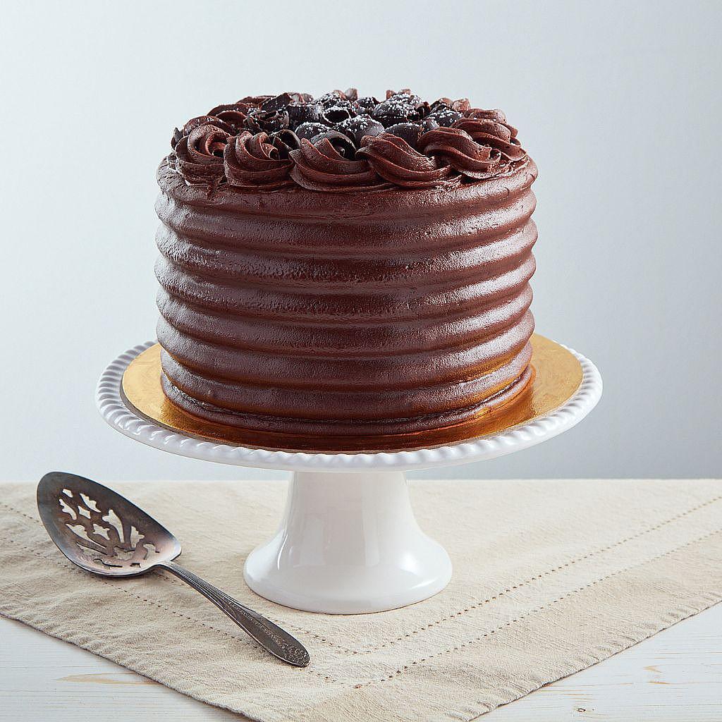 Six-inch chocolate cake with ribbed frosting, chocolate shavings, and powdered sugar on a white pedestal stand.
