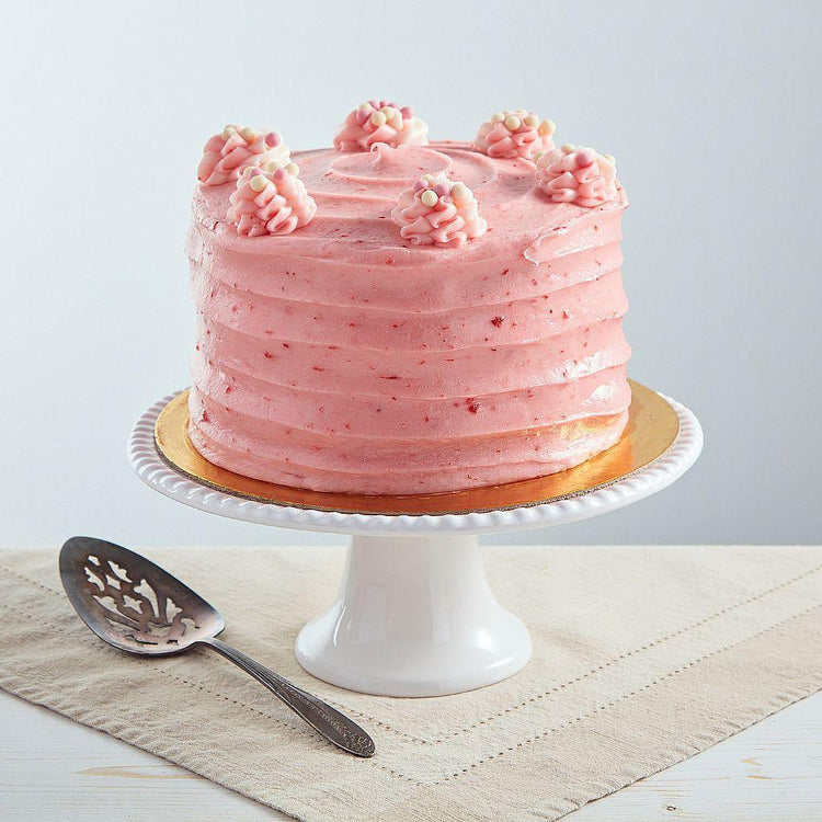 6-inch strawberry cake with pink cream cheese frosting, topped with piped swirls and sprinkles on a white pedestal stand.