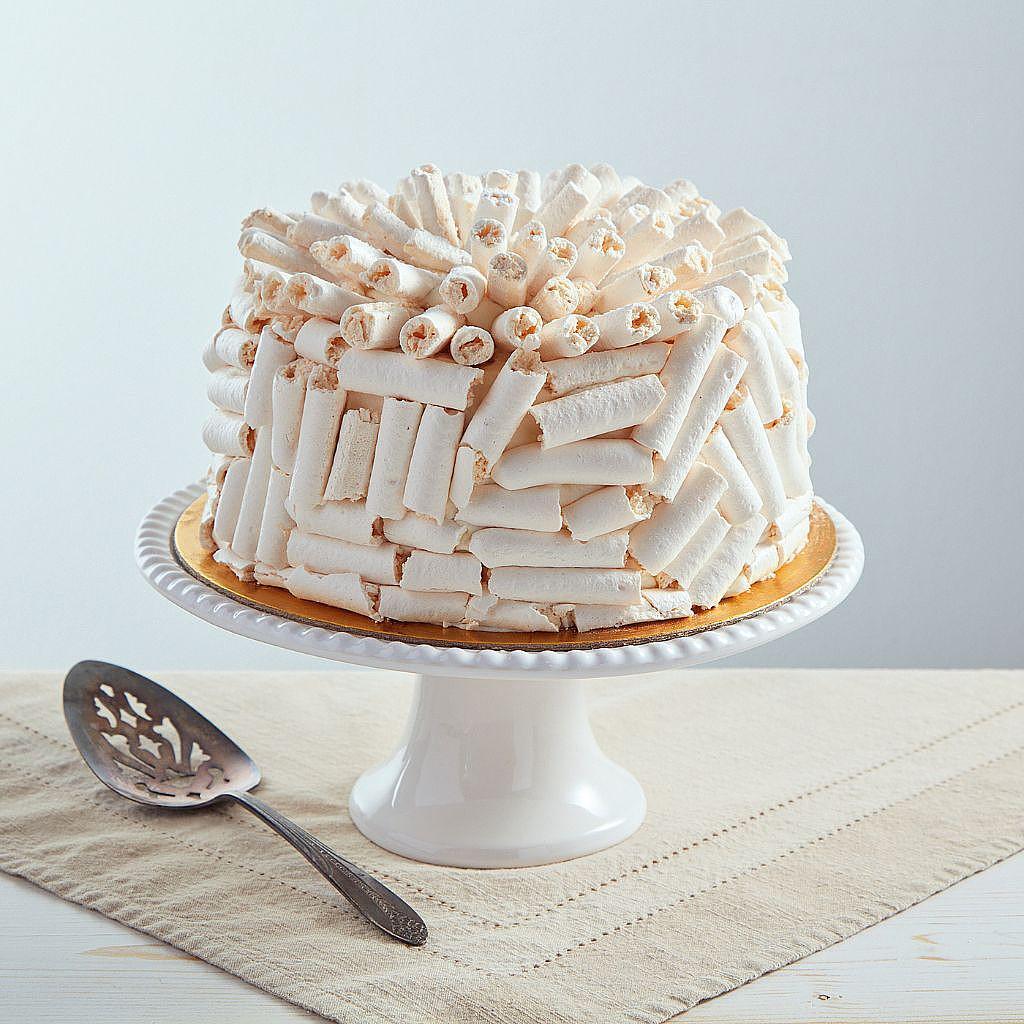 6-inch white chocolate Concorde cake covered in meringue curls on a white pedestal stand with a serving spatula.